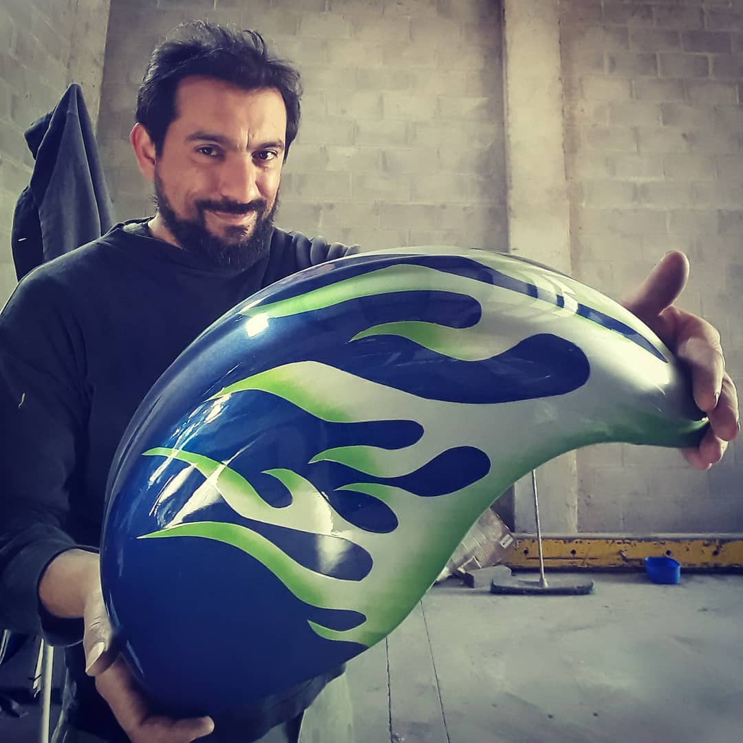 Persona sosteniendo el tanque de una moto pintado de forma perzonalizada.